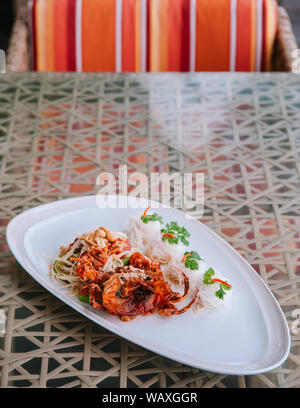 Som Tum - Thai spicy papaya salad with deep fried soft shell crab and rice noodle in white plate on table Stock Photo