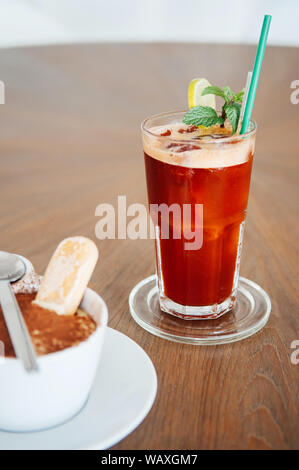 Cold iced red tea with lemon slice and mint in glass on wood table and some part of Panna Cotta in white cup Stock Photo