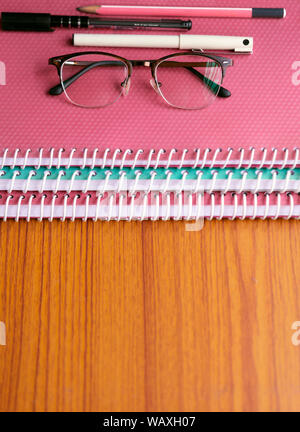 Books and assignments with teacher's glasses, pens and scale stacked on a wooden desk with space for text or copy. Concept for childhood education, sc Stock Photo
