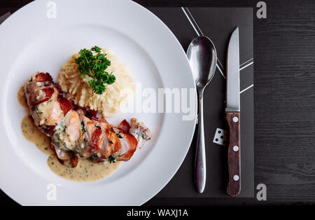 Roasted chicken crispy skin with white creamy sauce and mashed potato in white plate on black table with silverware set. Top view shot Stock Photo