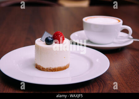 Creamy cheesecake with with raspberry and blueberry on white dish in bekery cafe. close up food shot Stock Photo