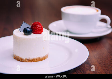 Creamy cheesecake with with raspberry and blueberry on white dish in bekery cafe. close up food shot Stock Photo