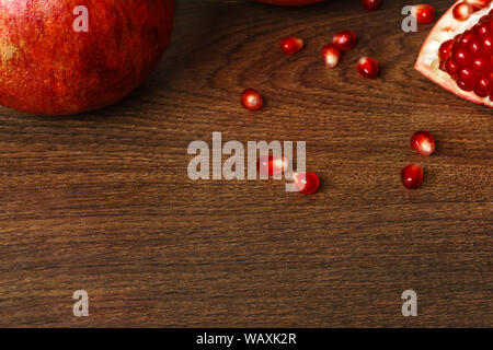 still life - red whole and cut pomegranate fruits and scattered seeds on a dark wooden tabletop Stock Photo