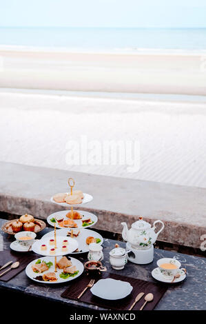 Beach side Afternoon tea set with tart and pastry bakery desserts on dark colour marble table in summer Stock Photo