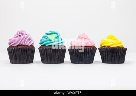 Four chocolate cup cakes with frosting or icing, pink, purple, yellow and blue with green leaf, photographed on a white background Stock Photo