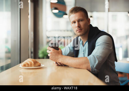 young handsome man having his croissant and drinking hot coffee for lunch in the cafe feeling calm Stock Photo