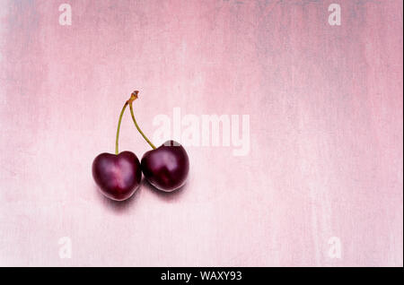 Concept of togetherness in a minimalist image of two cherries one heart shaped joined together against a pink background Stock Photo