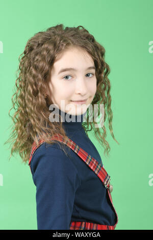 Portrait of adorable smiling schoolgirl with curl hair standing isolated on a green background. High resolution photo. Full depth of field. Stock Photo