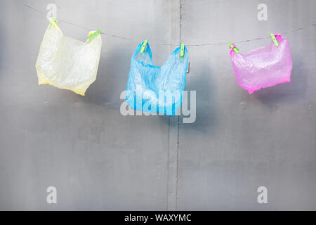 Three plastic bags hanging on the gray background. Concept of non-recyclable plastic pollution Stock Photo