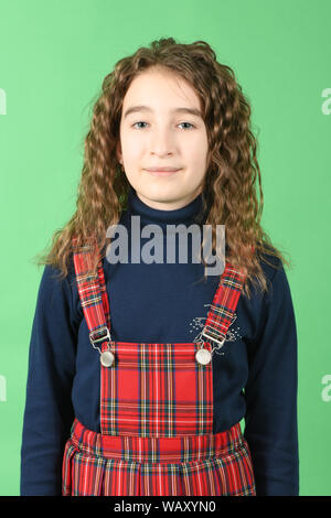 Portrait of adorable smiling schoolgirl with curl hair standing isolated on a green background. High resolution photo. Full depth of field. Stock Photo