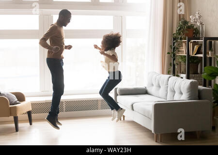 Happy African American father and little daughter jumping together
