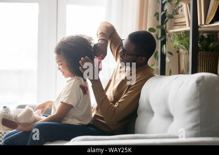 Caring African American father brushing combing preschool daughter hair Stock Photo