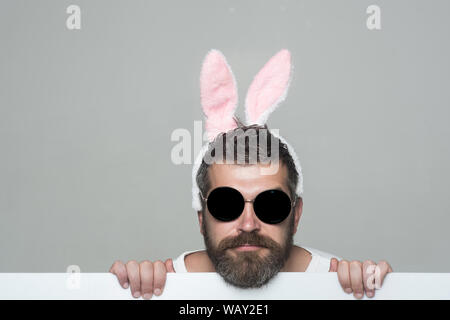 man with long beard in bunny ears and glasses on serious face with paper on grey background Stock Photo