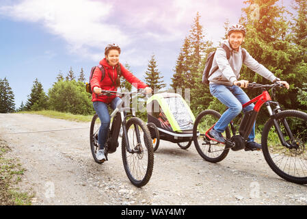 Family With Child In Trailer Riding Mountain Bikes In Alps Stock Photo