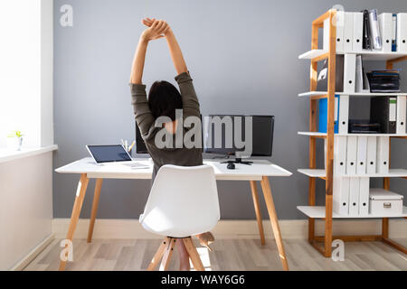 Rear View Of Young Businesswoman Stretching Her Arms In Office Stock Photo