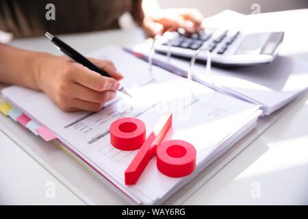 Close-up Of Red Percentage Symbol With Businessperson Calculating Bill Stock Photo