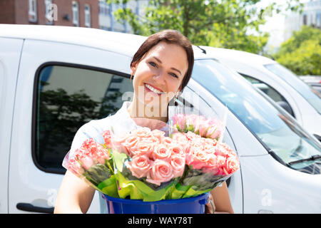 Portrait Of Happy Female Florist Holding Pink Flower Bouquet In Front Of Car Stock Photo