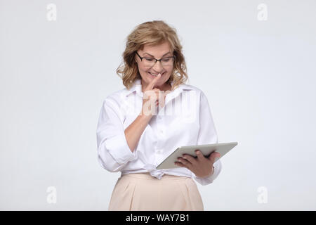 Senior woman reading interesting message via tablet Stock Photo