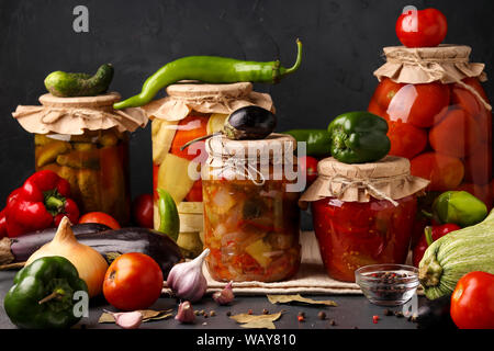 Different pickled vegetables in glass jars for long-term storage: salad with eggplant, peppers, cucumbers, tomatoes and mixed vegetables against a Stock Photo