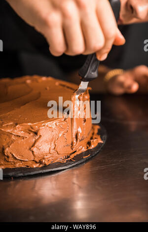 Smoothing chocolate cream on cake by spatula Stock Photo