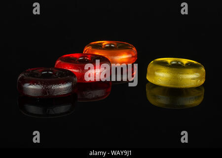 Group of four whole colourful hard candy dark red cherry orange yellow isolated on black glass Stock Photo