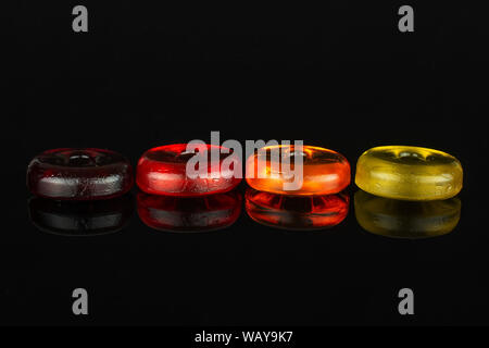 Group of four whole colourful hard candy dark red cherry orange yellow in line isolated on black glass Stock Photo