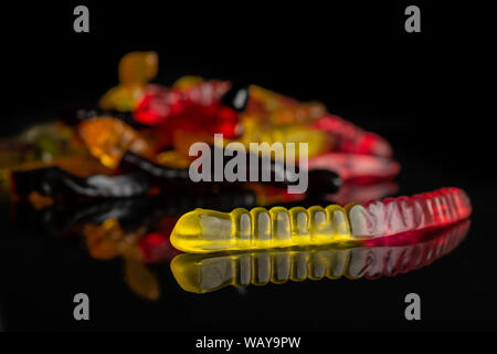 Lot of whole colourful jelly worm candy front focus isolated on black glass Stock Photo