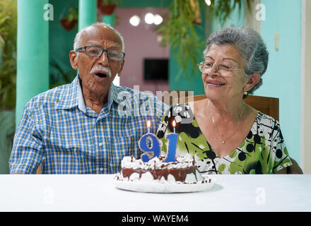Elder couple with a cake on a table and the number 91 on the cake and two burning candle Stock Photo