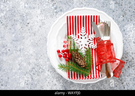 Christmas table setting with empty festive white plate and cutlery with Xmas decorations, snowflake, cone, Xmas tree branches and New Year napkin. Hol Stock Photo