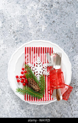 Christmas table setting with empty festive white plate and cutlery with Xmas decorations, snowflake, cone, Xmas tree branches and New Year napkin. Hol Stock Photo