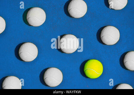 Creative composition made with yellow tennis ball and white balls on blue background. Stock Photo