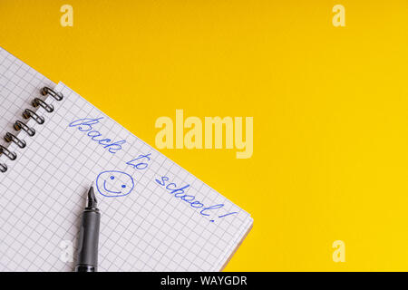 The inscription back to school and smile on a squared notebook and ink pen on a yellow background Stock Photo