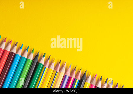 Many sharpened colored pencils laid out on a yellow background. Copyspace Stock Photo
