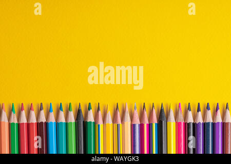 Many sharpened colored pencils laid out on a yellow background. Copyspace Stock Photo