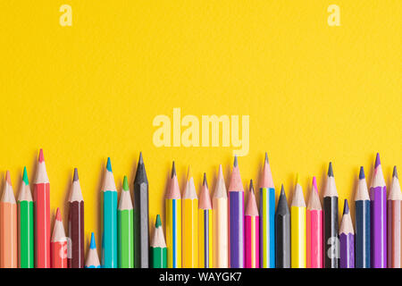 Many sharpened colored pencils laid out on a yellow background. Copyspace Stock Photo