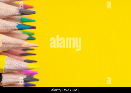 Many sharpened colored pencils laid out on a yellow background. Copyspace Stock Photo