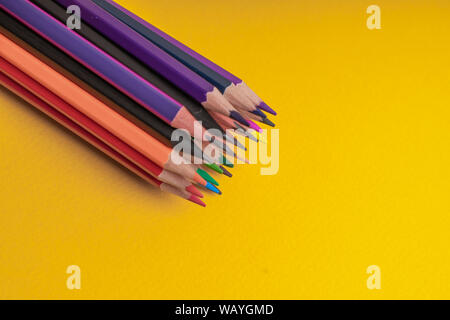 Many sharpened colored pencils laid out on a yellow background. Copyspace Stock Photo