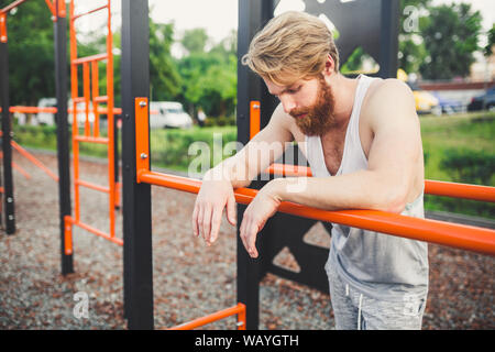 Portrait of Tired Athlete at Gym. Tired man hanging from the bar. Exhausted athlete working out in gym. Time to rest. Long workout is over. Muscular Stock Photo