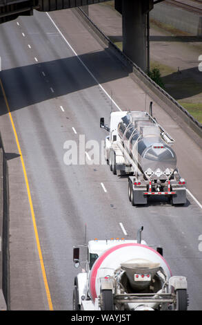 Big rig day cab white semi truck for local delivery transports liquid cargo in a stainless steel tank semi trailer running on the wide highway in fron Stock Photo