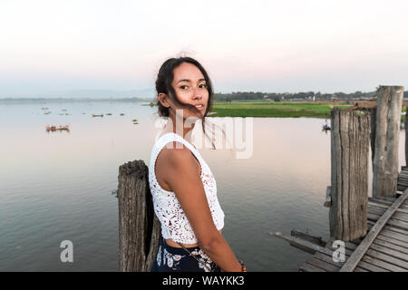 Wide angle picture of brunette woman posing at U Bein Bridge during sunset in Mandalay, Myanmar Stock Photo