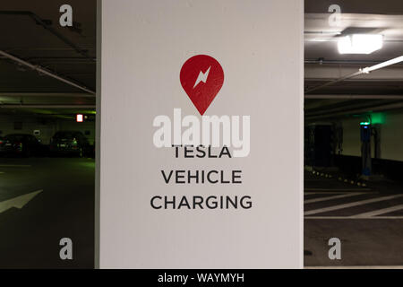 Tesla Supercharger logo and Tesla Vehicle Charging text on post in parking garage in-front of Tesla Supercharger Station. Stock Photo