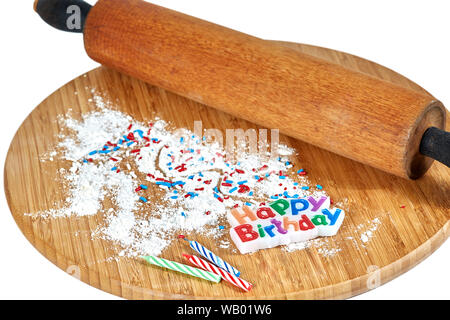 A wooden rolling pin on a bamboo cutting board with white flour and red, white and blue sprinkles and birthday candles on the board isolated on white Stock Photo