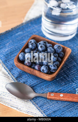 Blueberries in a wood bowl on top of blue and white napkin with a spoon Stock Photo