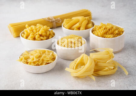 Various types of dry pasta in bowls on light gray background. Ingredients for cooking. Stock Photo