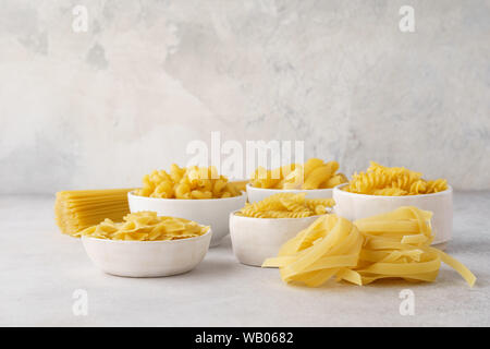 Various types of dry pasta in bowls on light gray background. Ingredients for cooking. Copy space. Stock Photo