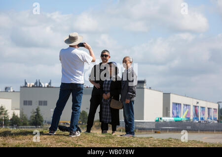 A family poses for a photo in front of the Boeing Everett Factory in Everett, Washington on August 22, 2019. The final assembly plant, the largest building in the world by volume, is where majority of Boeing’s wide-body airplanes are assembled including the 747, 767, 777 and 787. Stock Photo