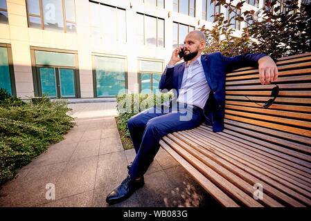 A successful young man is sitting on a bench near a business center. Stock Photo