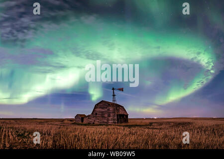 Swirl of bright Northern Lights over vintage barn, bins, windmill and stubble in Saskatchewan, Canada Stock Photo