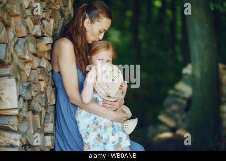 beautiful long-haired mother in a long blue dress in sunny summer forest walks with his beautiful daughters Stock Photo