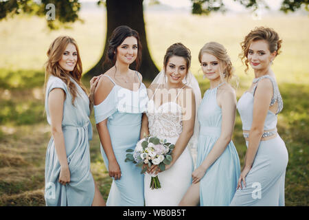 elegant and stylish bride along with her four girlfriends in blue dresses standing in a park Stock Photo